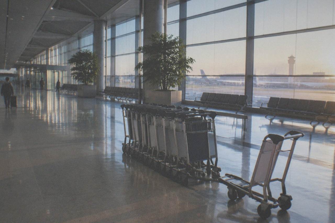 Empty airport terminal concourse with polished floor and departure boards above a row of baggage trolleys