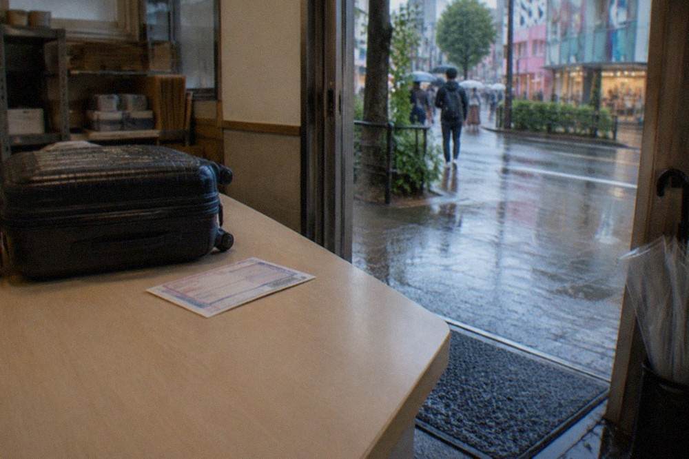 A convenience store counter in Tokyo with a parcel shipping slip and a small suitcase resting beside it.