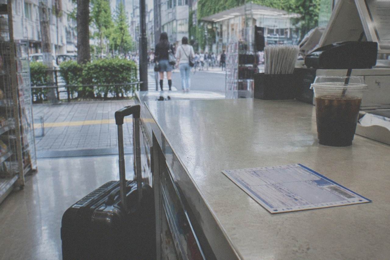 A convenience store counter in Tokyo with a parcel shipping slip and a small suitcase resting beside it.