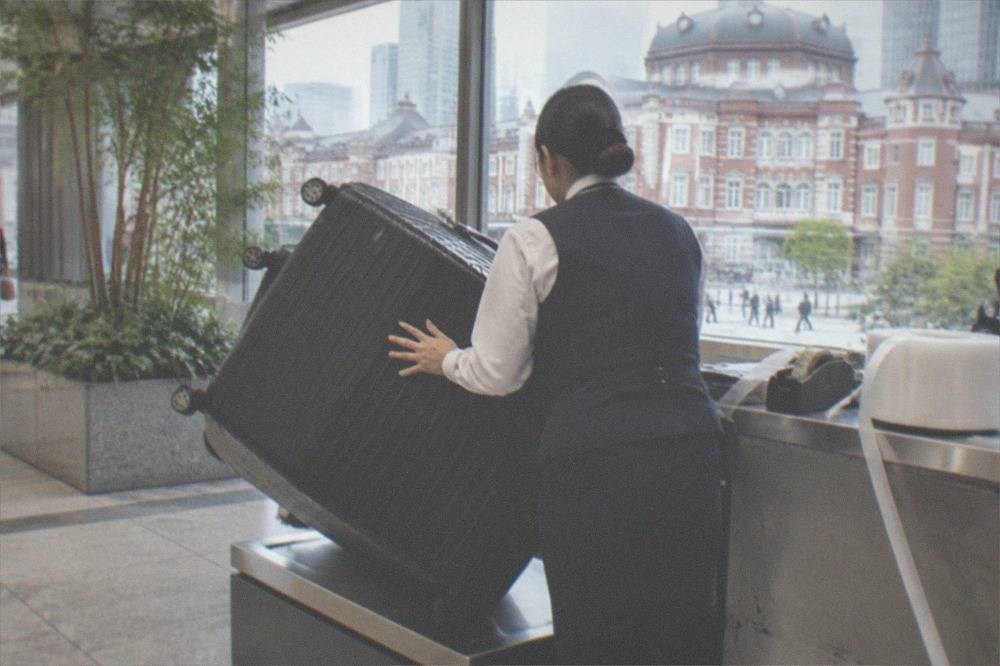 A large suitcase being handed over at a luggage forwarding counter in a Japanese airport