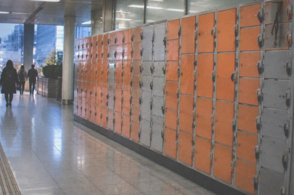 Rows of orange and grey coin lockers filling a wall inside a Tokyo station corridor