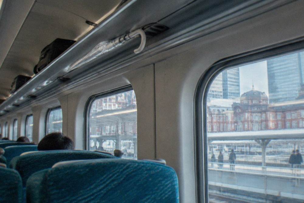 Interior of a Shinkansen car with deep overhead luggage racks above reclining seats