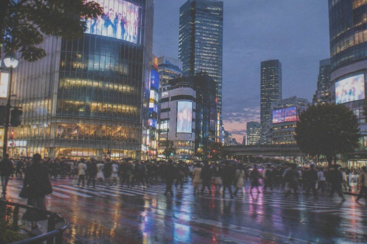 A busy Tokyo intersection at dusk with glowing signs and a pedestrian scramble crossing