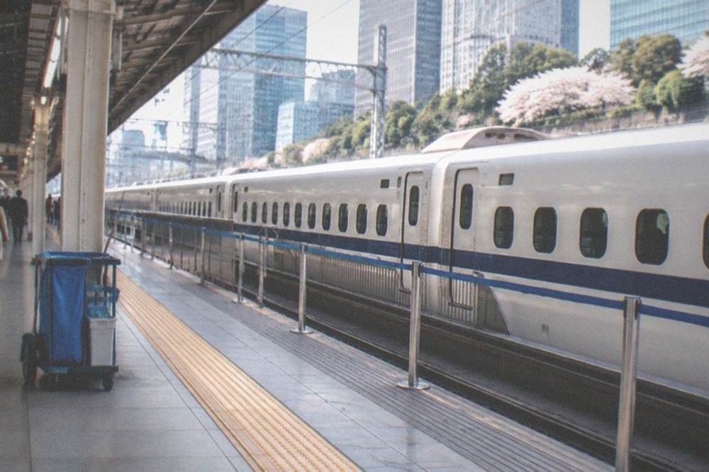A high-speed train platform with a long white train stopped alongside a roped queue area.