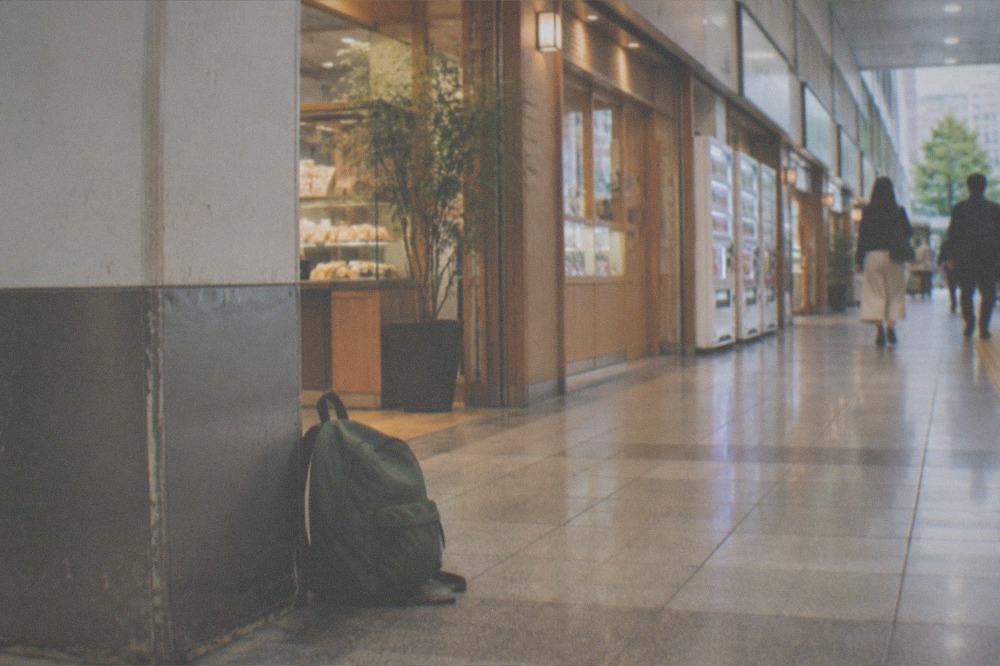 A small backpack resting on a wooden bench inside a bright station shopping arcade.