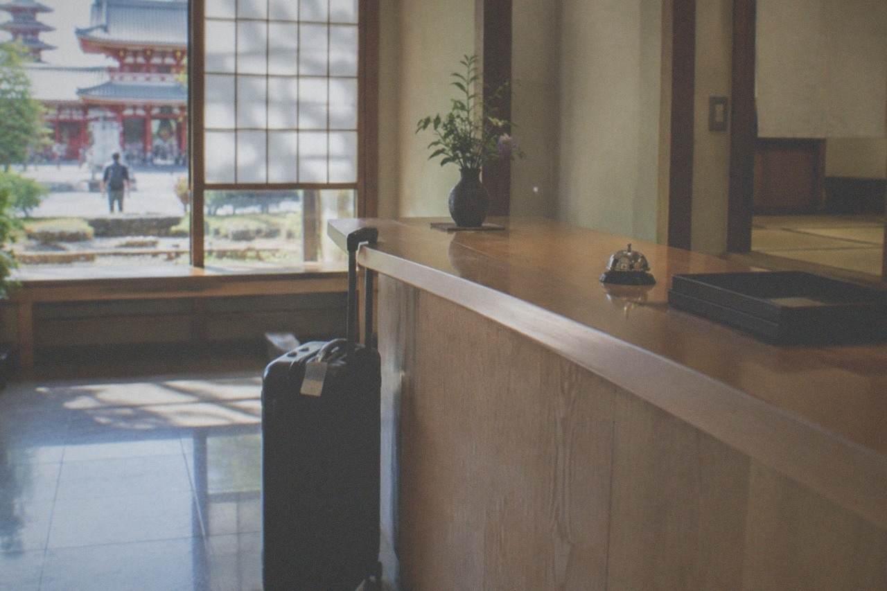 A labelled suitcase standing beside a hotel front desk counter in a bright lobby.