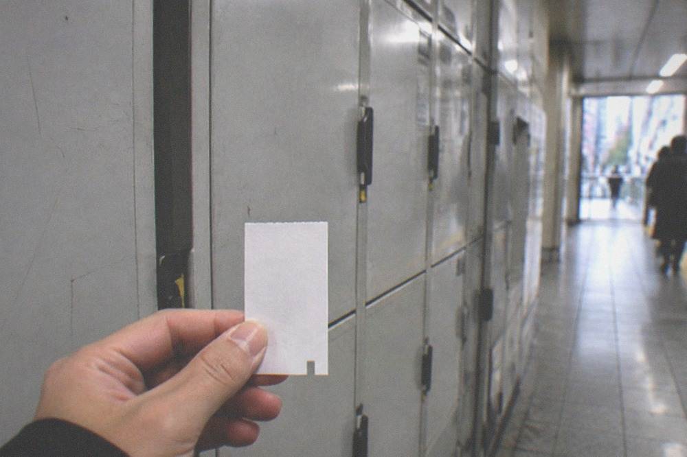 A small paper locker ticket held in front of a closed grey locker door