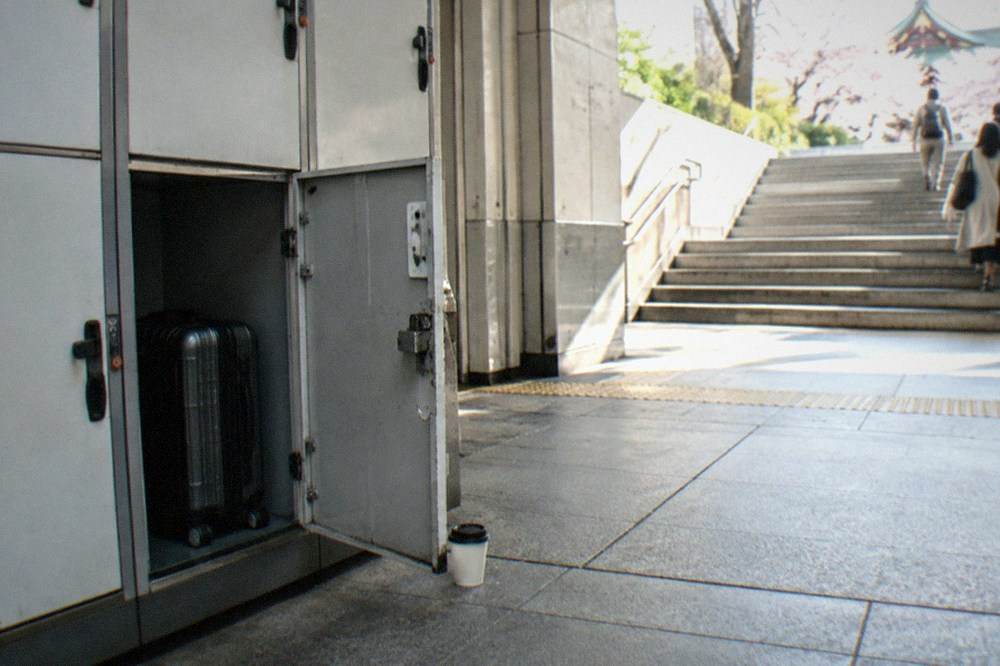 A coin locker door standing open with a small suitcase being placed inside