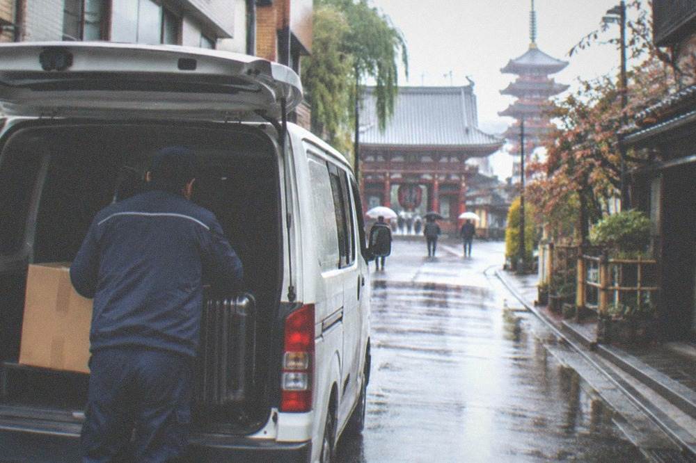 A Yamato delivery driver loading a cardboard box and a suitcase into a van in Tokyo