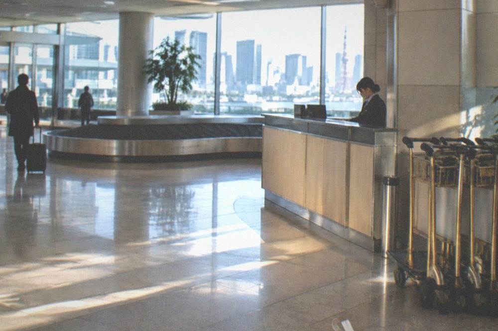 An airport arrival hall with a staffed baggage counter and trolleys beside the desk