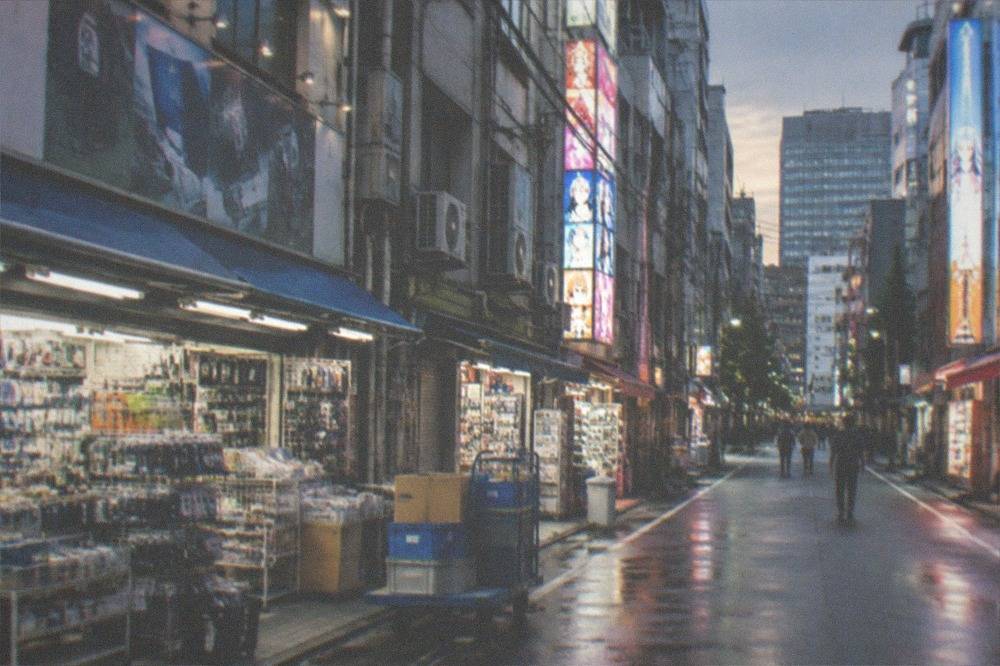 An electronics shopping district street with bright signboards above small shops