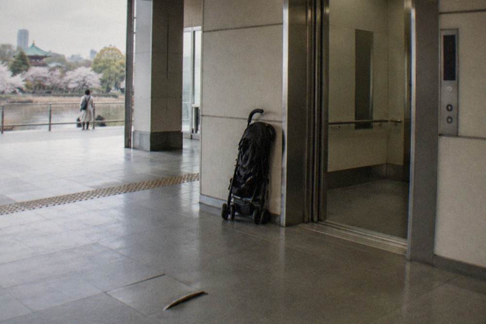 A wide station lift lobby with open doors and a folded stroller parked beside the wall