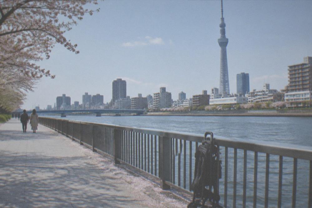 A wide riverside walkway with smooth paving and an empty parked stroller by a railing